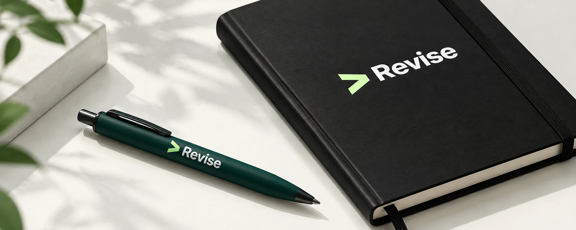 Dark green Revise pen next to a black notebook with the Revise logo on a sunlit desk