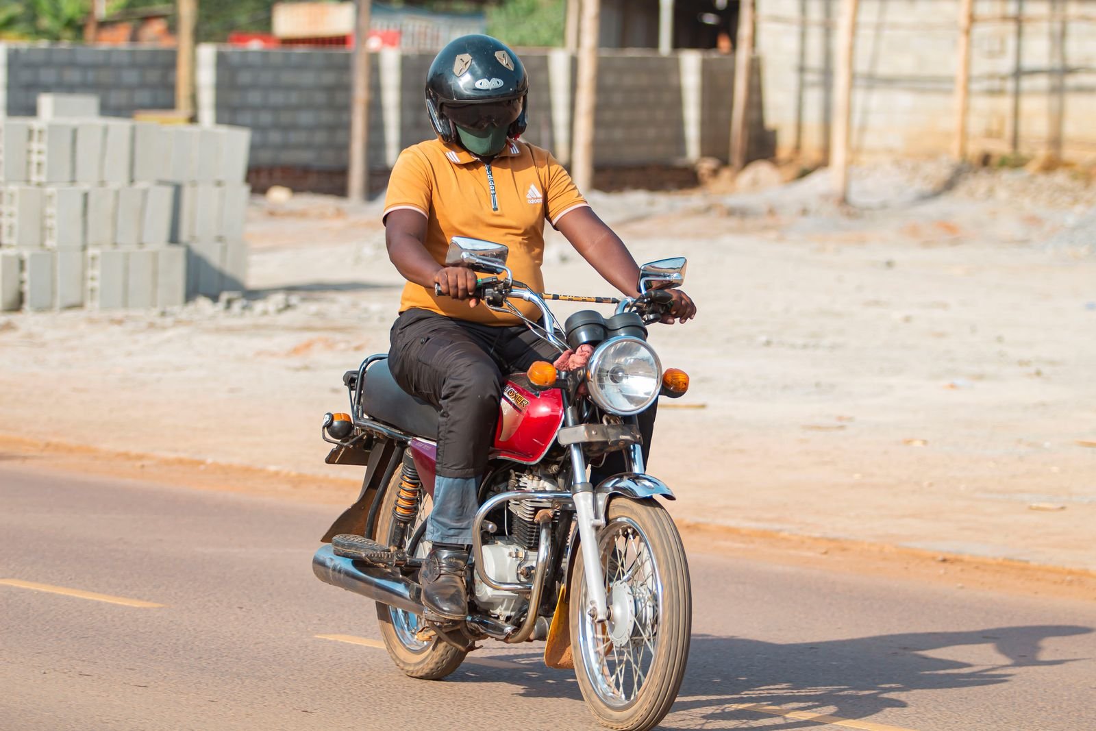 Motorcycle rider in a helmet on a sunlit street in Kampala, Uganda