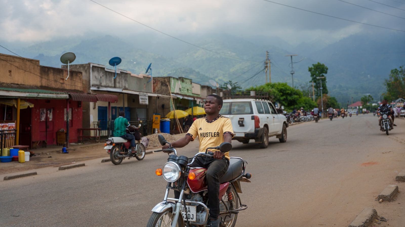 Motorcyclist on a busy street in a Ugandan town with hills behind