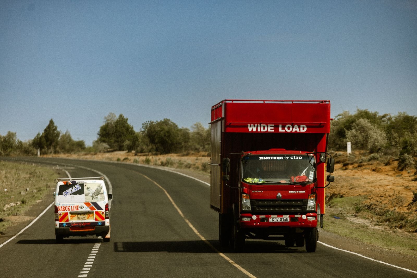 A red wide-load truck and a van on an open highway in Africa